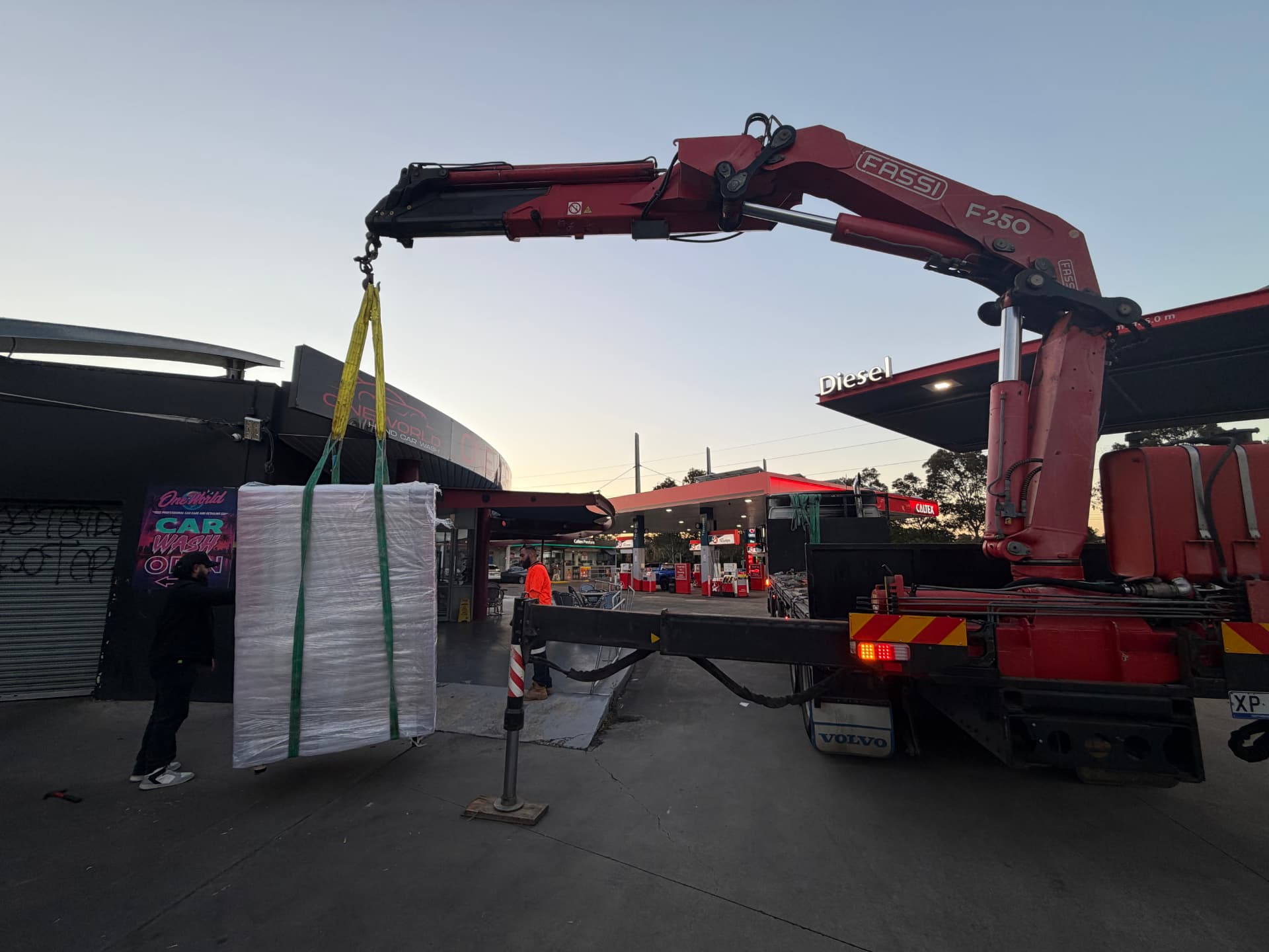 Everest Transport Fassi F250 crane truck lifting a wrapped pallet at a Sydney service station forecourt